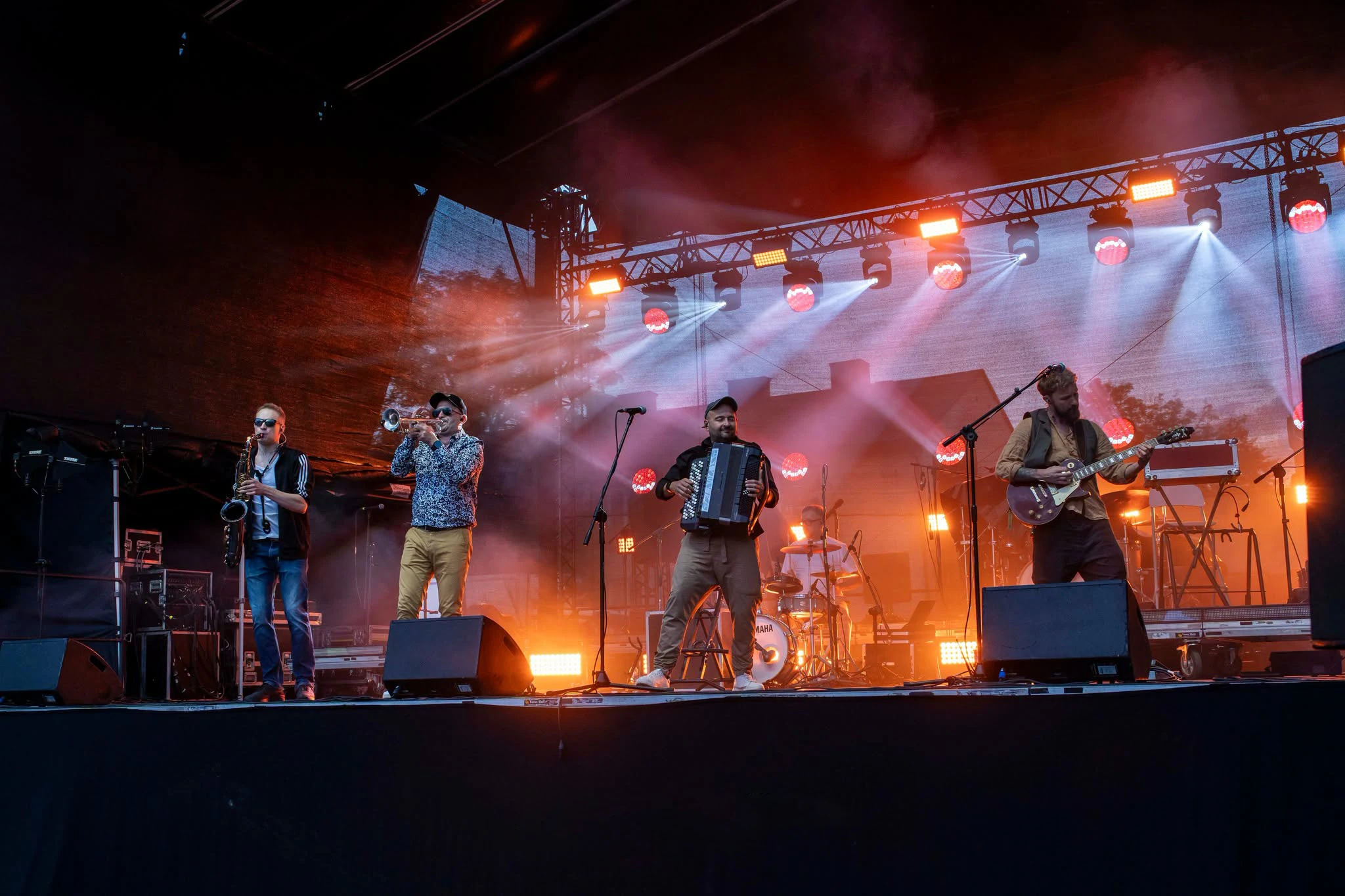 Pięciu muzyków Propabanda na scenie - saksofon, trąbka, akordeon, perkusja i gitara, w czerwono-białym świetle reflektorów