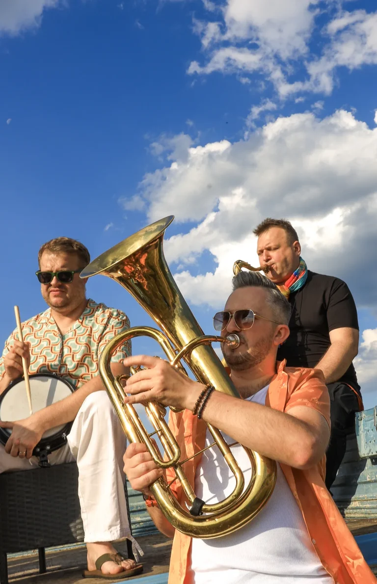 Dwóch muzyków Propabanda z trąbką i akordeonem grających na tle błękitnego nieba
